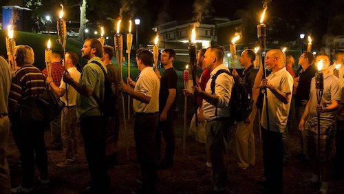 a far right rally taking place in the USA. The men are all holding torch flames, marching at night