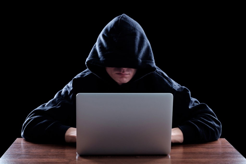 Hacker in a dark hoody sitting in front of a notebook. Cybersecurity concept. Dark background
