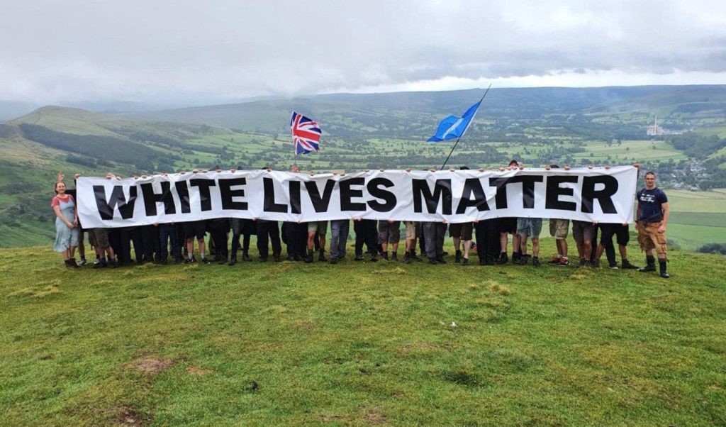 a group of racial nationalists standing behind a banner which says "white lives matter"