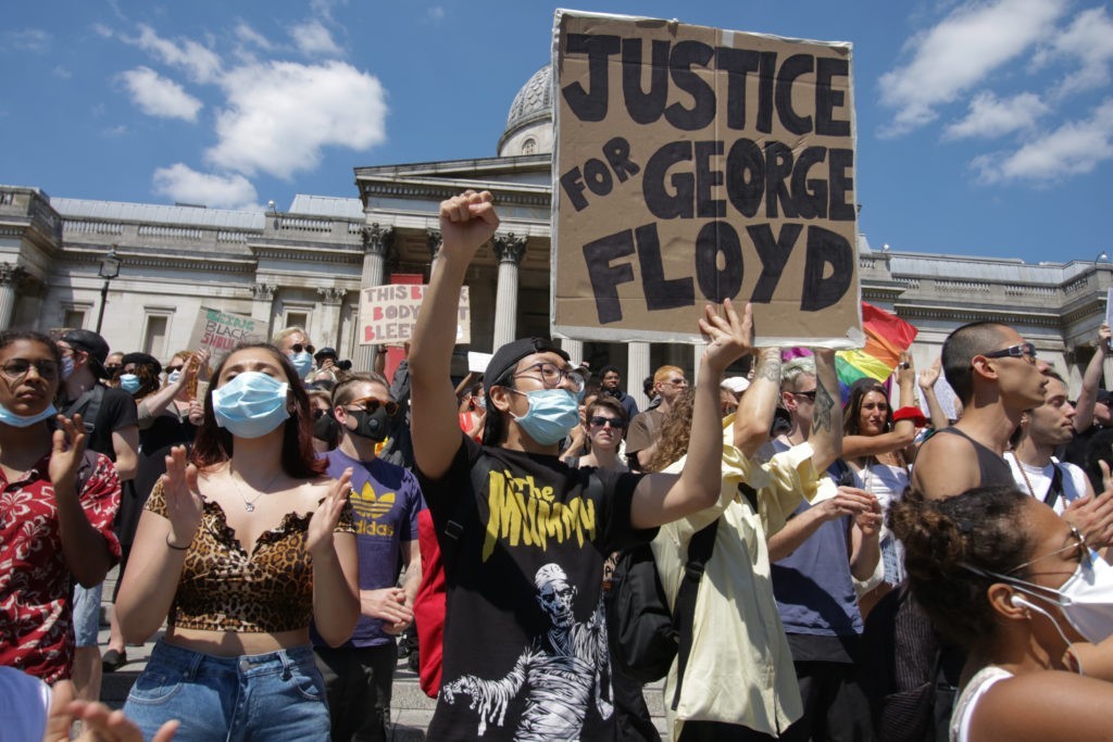 Numerous of people taking part in last year's Black Lives Matter protest outside Trafalgar Square, London. A man is holding a sign that says "Justice for George Floyd"