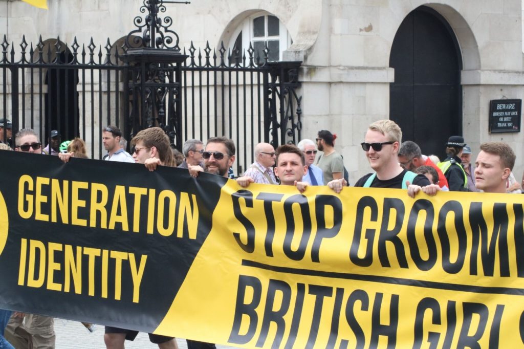 Members of Generation Identity UK holding a banner. Banner says "Stop grooming British girls."