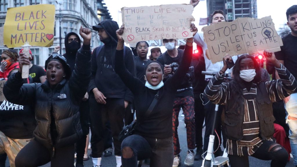 Young people protesting in the Black Lives Matter march in London. 3 of them are holding placards